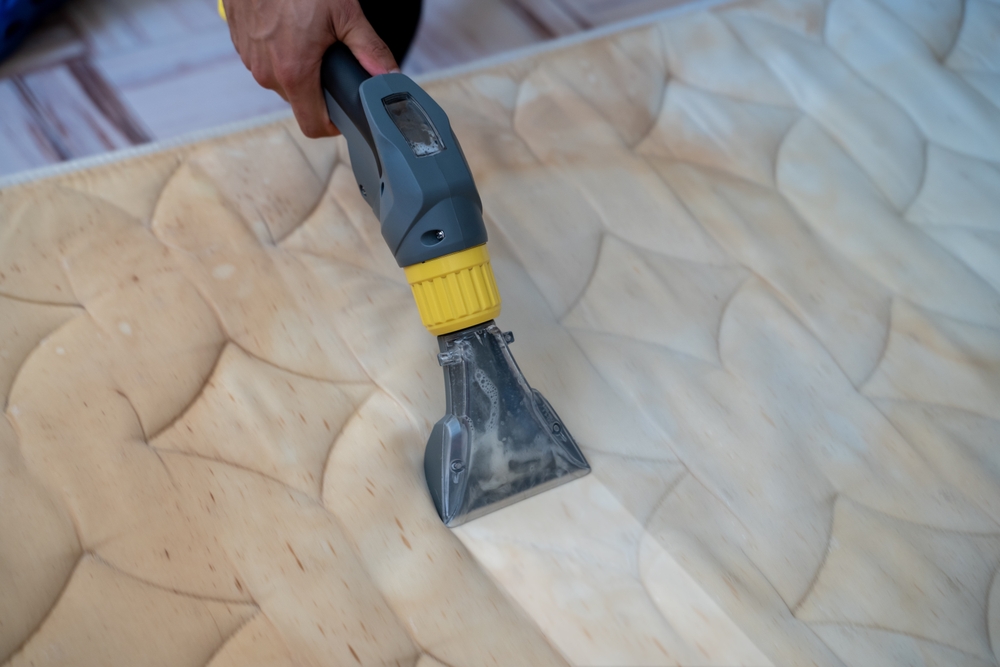 alt="Close-up of a hand using a vacuum cleaner with a specialized attachment on a mattress, showcasing a cleaning method for removing bed bugs and ensuring hygiene."