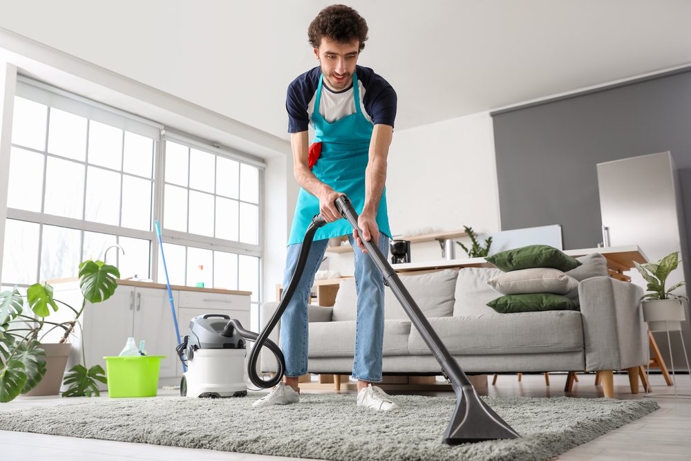 Young man vacuuming the carpet in a Dubai home, showcasing the effectiveness of residential carpet cleaning services.