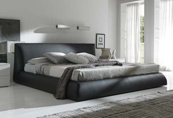 A stylish king-size mattress on a sleek black frame with decorative pillows and a cozy gray throw in a bright, contemporary bedroom, perfect for expert mattress cleaning services in Dubai.