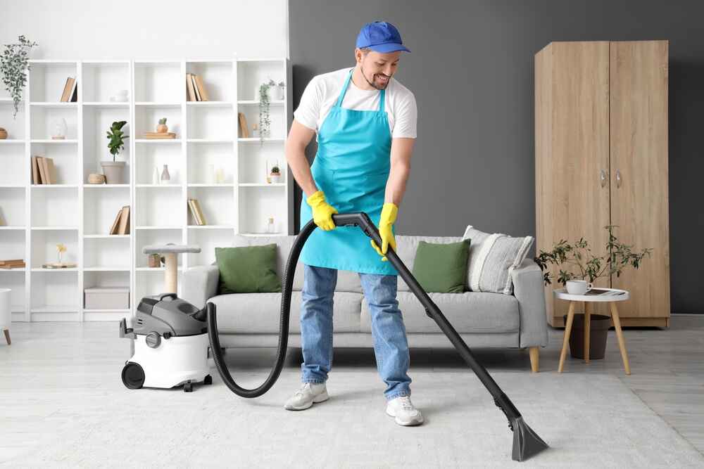A cleaner in uniform performing professional carpet cleaning in a residential living room in Dubai with advanced equipment.