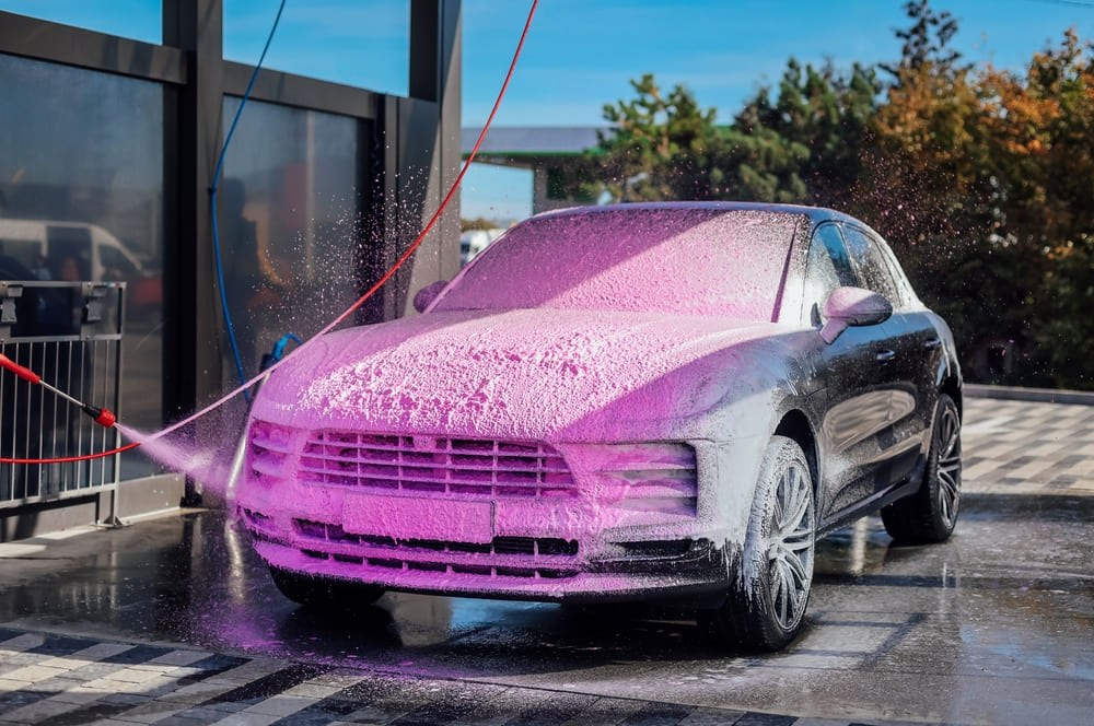 A modern SUV is covered in pink foam during a professional car deep cleaning service in Dubai. High-pressure wash removes dirt and grime for a spotless finish.