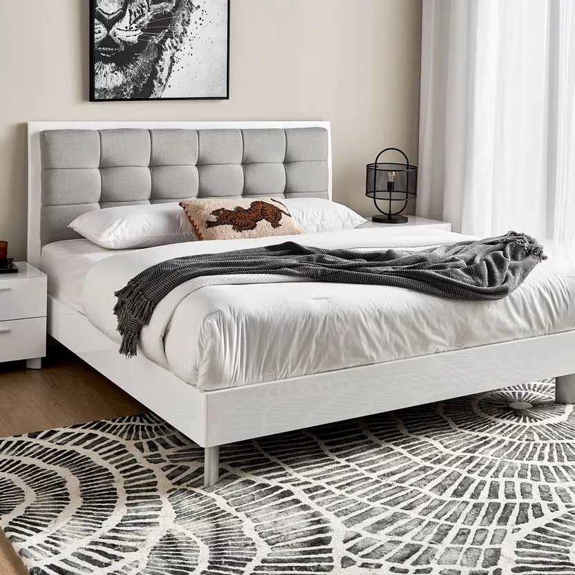 Modern white queen bed with a gray tufted headboard, adorned with pillows and a cozy throw blanket, placed on a patterned rug in a minimalist bedroom with a framed lion artwork on the wall.
