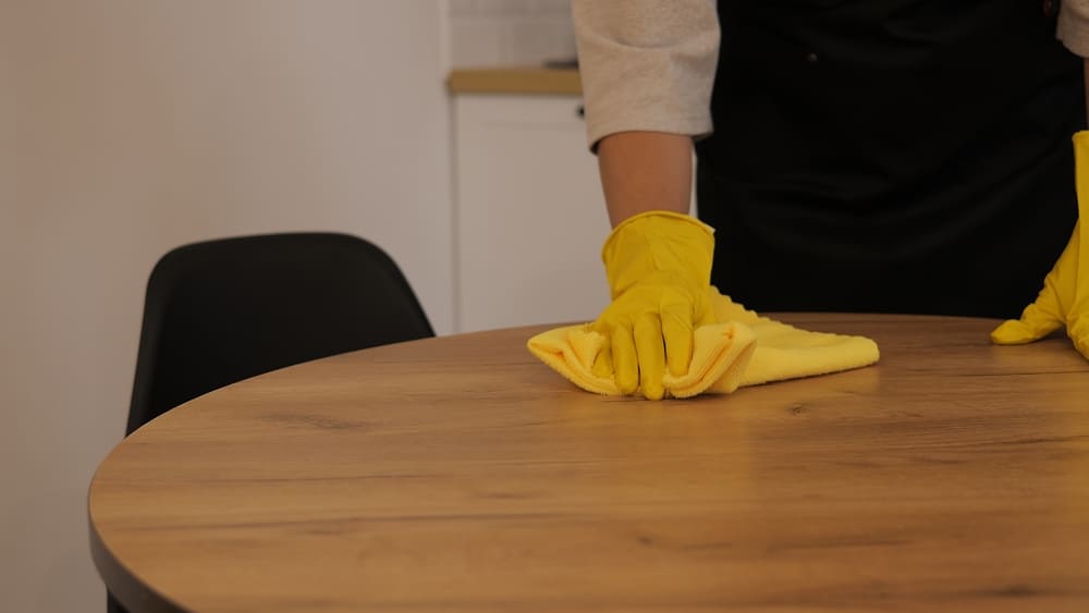 A woman wiping a table with a cloth, showcasing surface-level cleaning as part of regular cleaning tasks.
